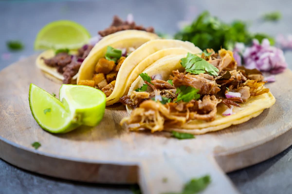 Three street tacos with lime on a wooden plate